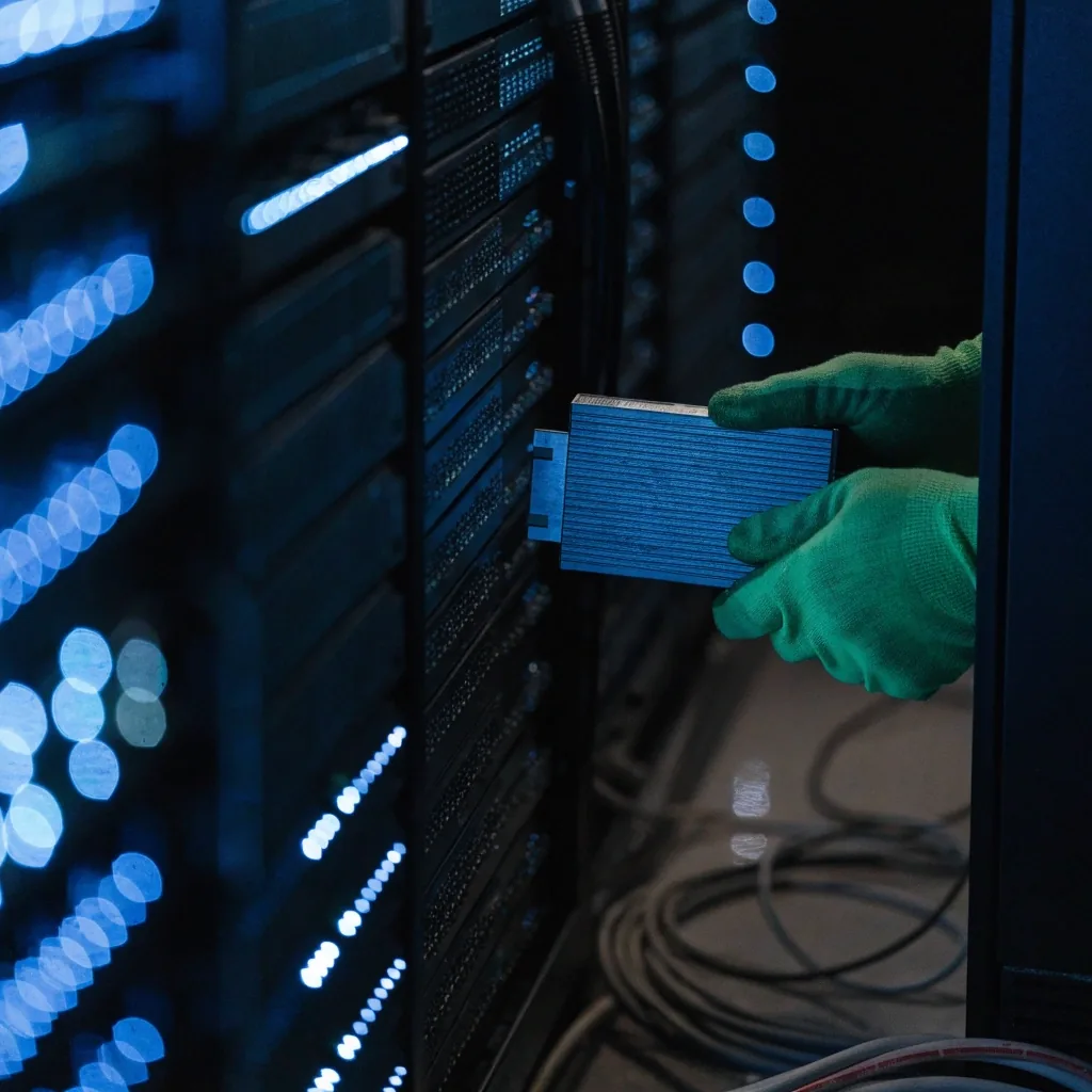 Server-room aisle at night with cold blue rack light and a hand reseating a cable